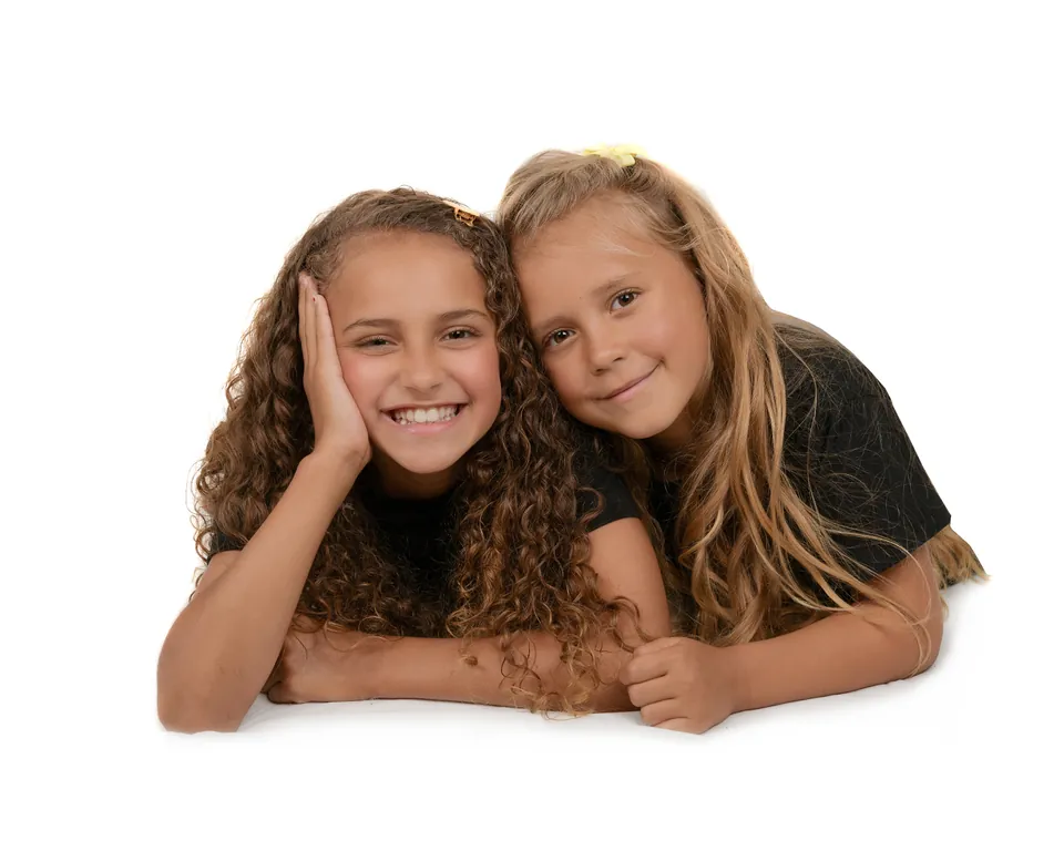 Two girls lying on white, chins propped on their hands, smiling