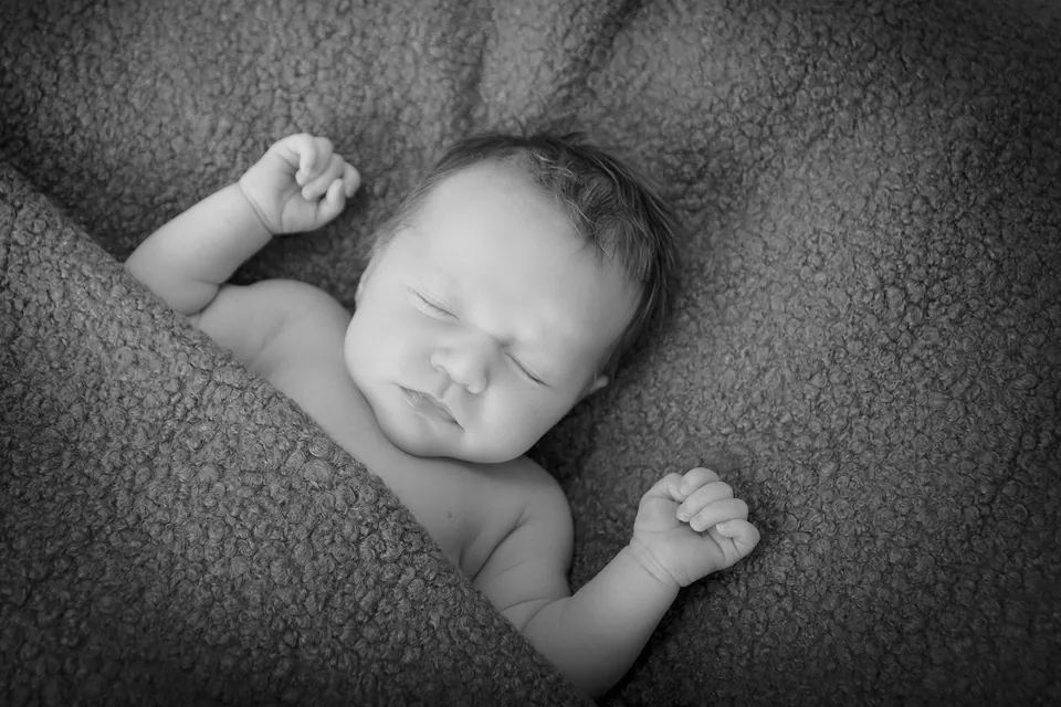 Black-and-white portrait of a sleeping newborn nestled in a deep fleece blanket