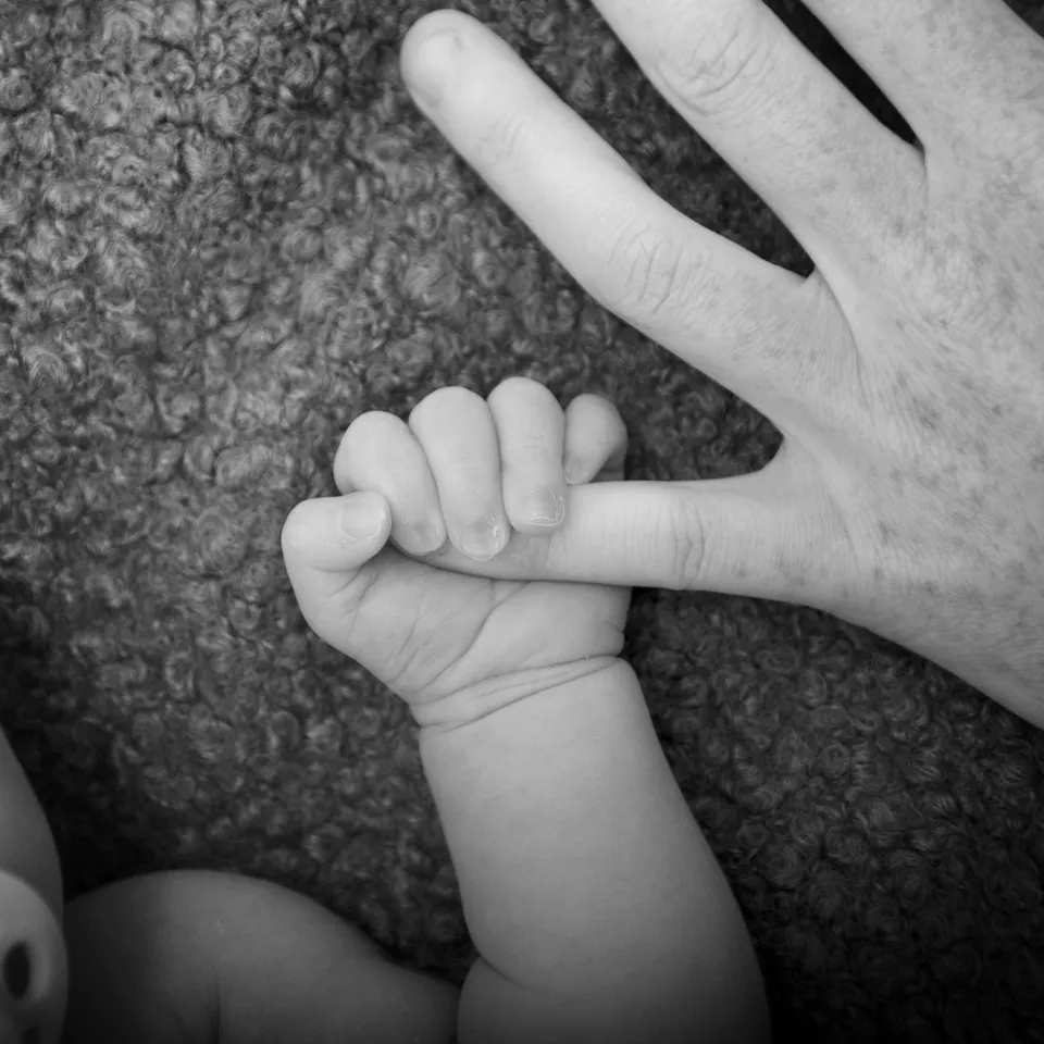 Black-and-white detail of a baby's fist curled around an adult's finger