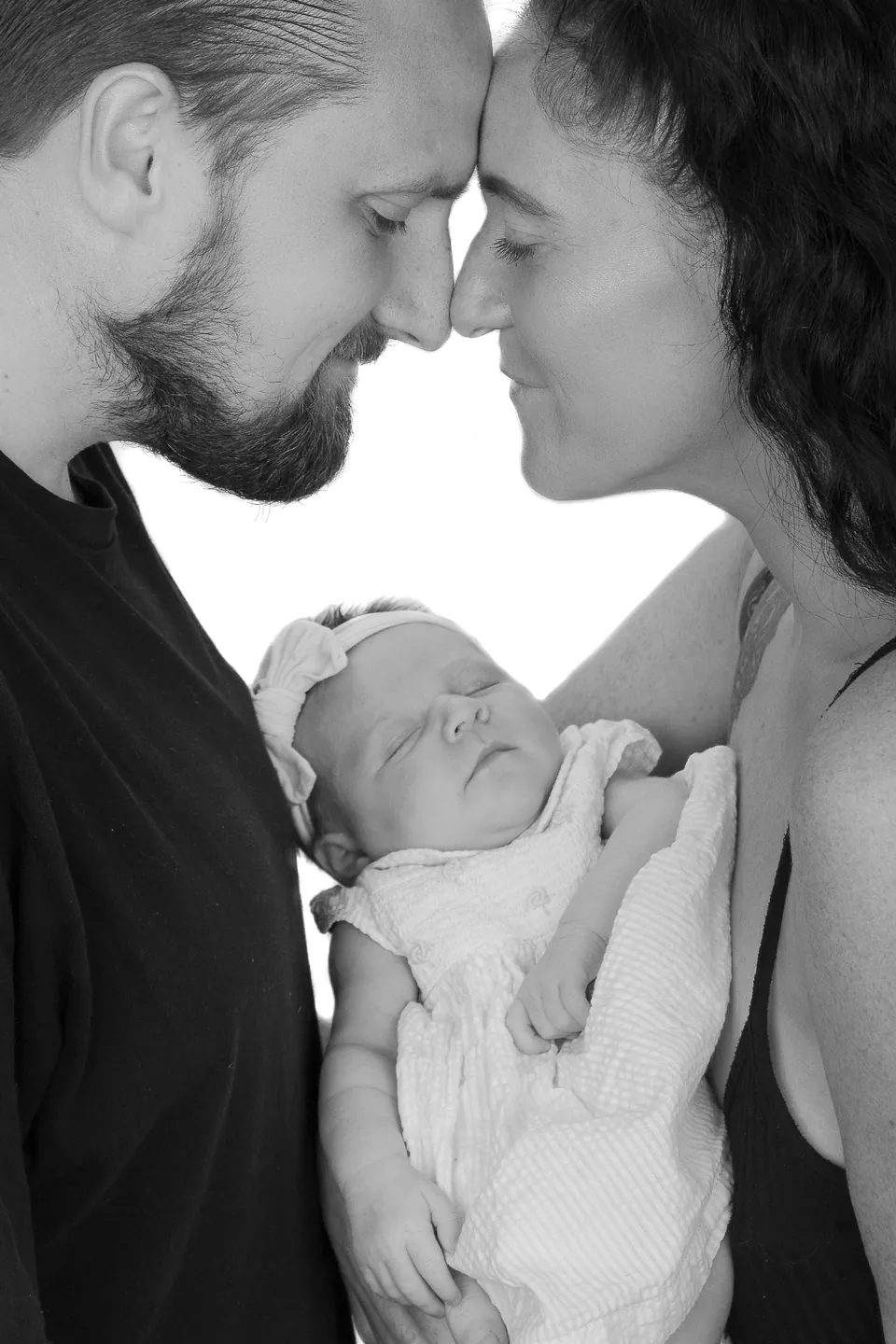 Black-and-white portrait of a couple forehead to forehead, holding their newborn