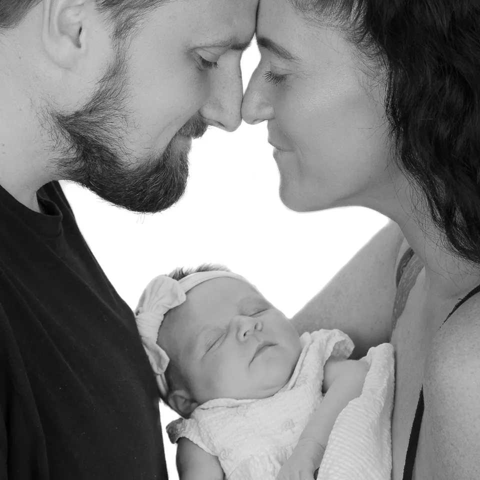 Square black-and-white crop of a couple holding their newborn between them
