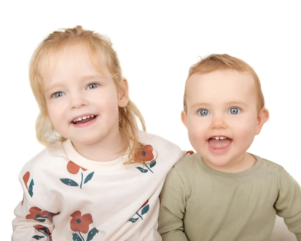 Two young children side by side on white, both laughing at the camera