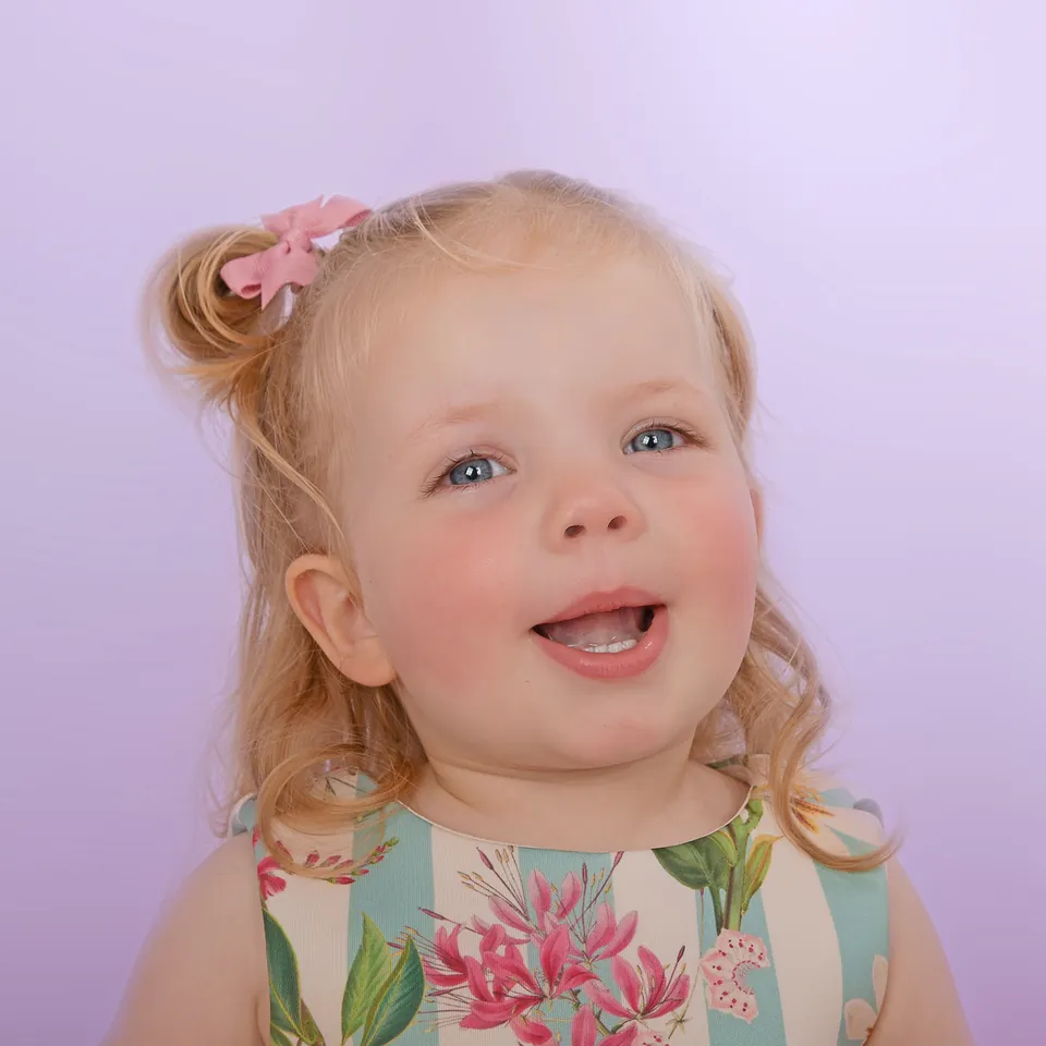 Close studio portrait of a laughing toddler in a floral striped dress