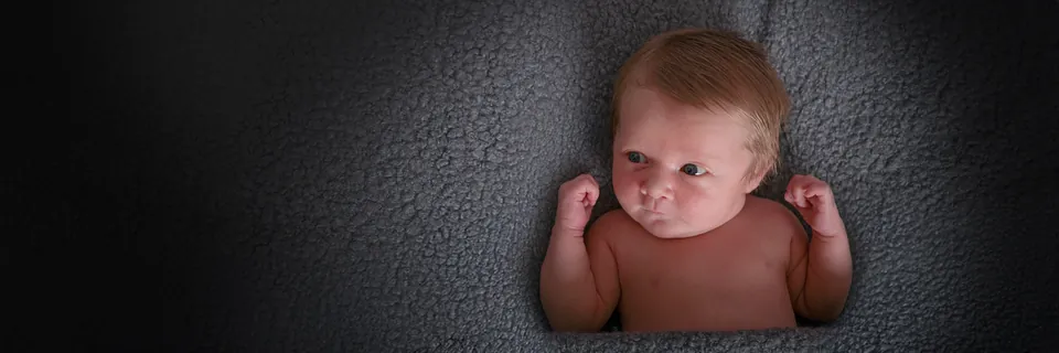 Panoramic frame of a wide-awake newborn spotlit on a dark grey blanket