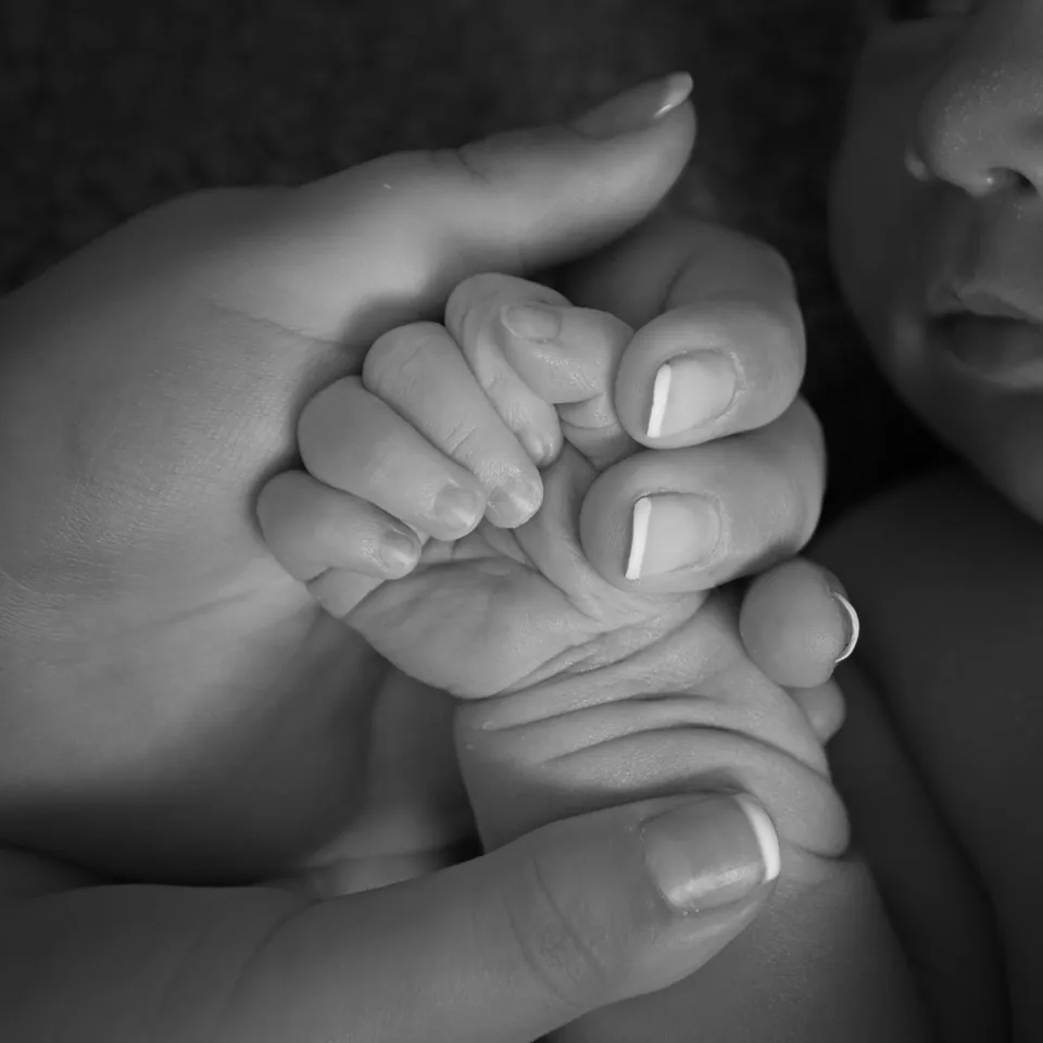 Black-and-white detail of a newborn's hand held between two adult hands