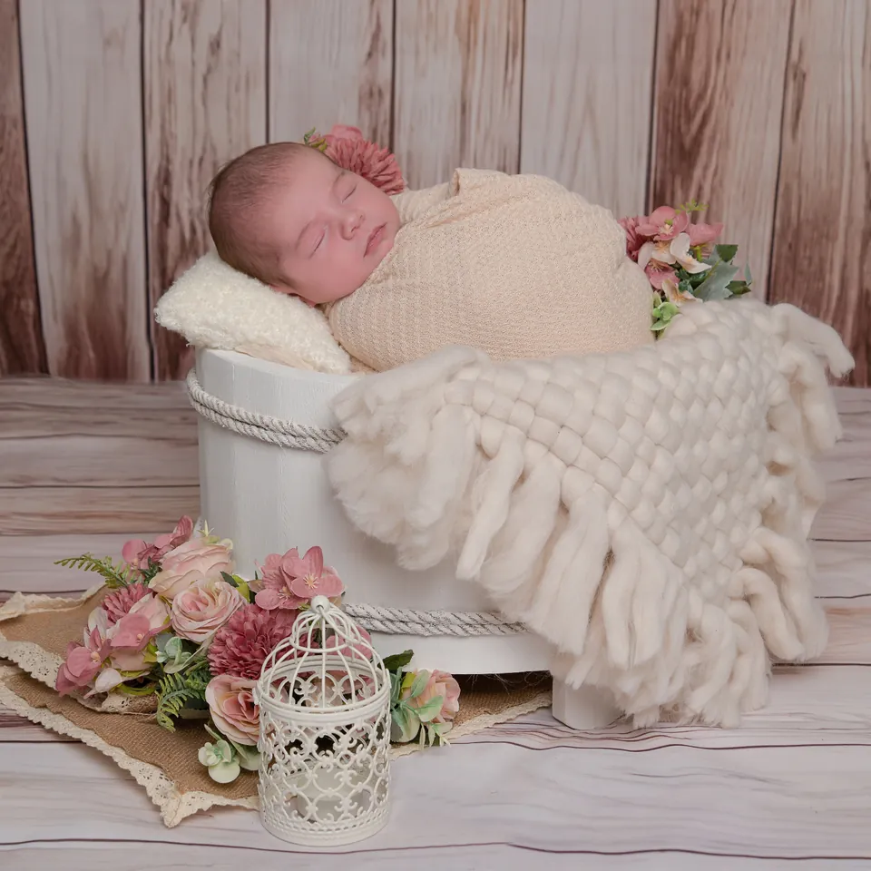 Newborn asleep in a white tub on a rustic wooden set dressed with pink blooms