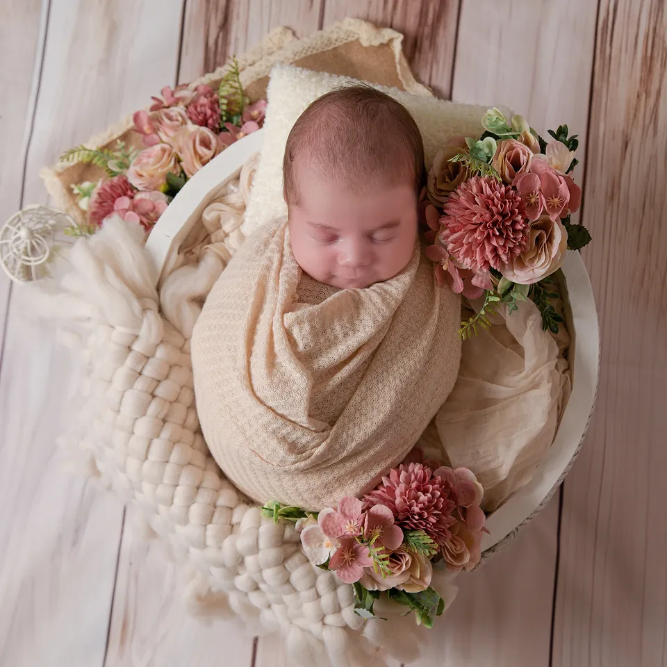 Newborn wrapped in cream, seen from above in a bowl ringed with pink dahlias